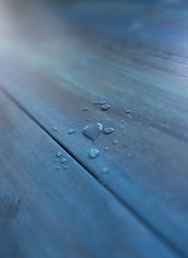 Gotas de agua sobre madera azul tratada, mostrando impermeabilización efectiva por Grupo IMAP en Pereira